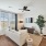 Living room with floor to ceilings, wood plank flooring, ceiling fan, tv mounted on wall, couch, lamp, dining table against wall with two framed photos