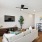 Living room with wood plank flooring, ceiling fan, tv mounted on wall, couch, lamp, dining table against wall with two framed photos